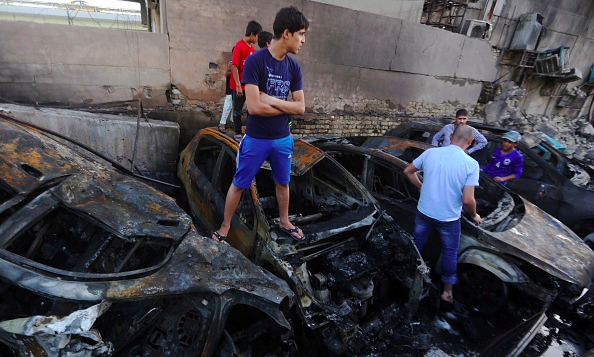 Iraqi men inspect charred vehicles at a parking-lot at the Beirut Square east of the capital Baghdad following an explosion