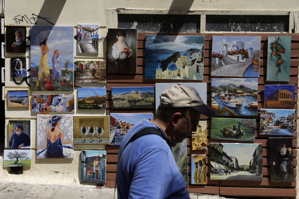 A man passes a shops with paintings of scene of Greece in the Plaka tourist district of Athens on Tuesday