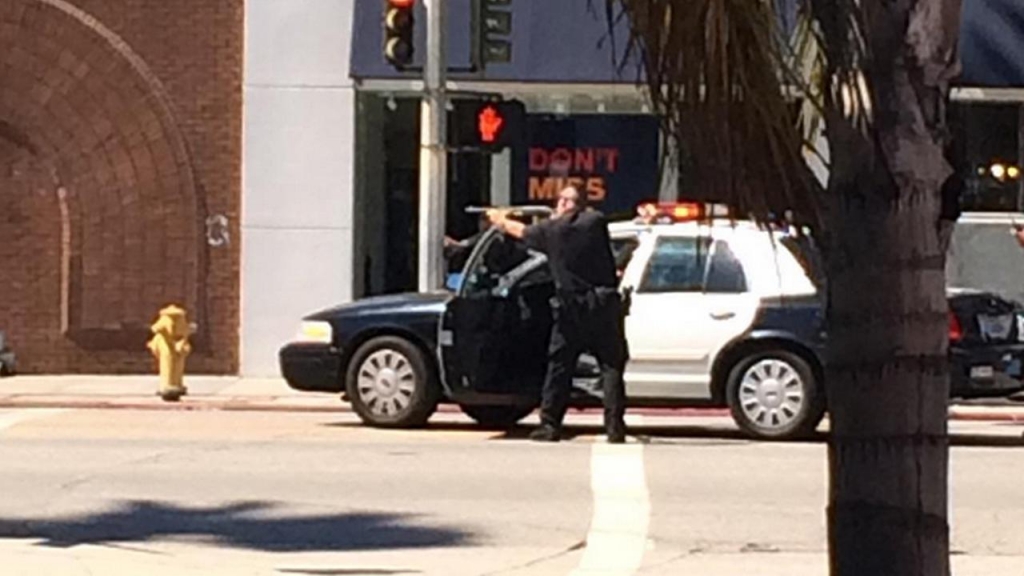 A police officer draws his gun on Ventura Boulevard near Laurel Canyon Boulevard in Studio City on Friday