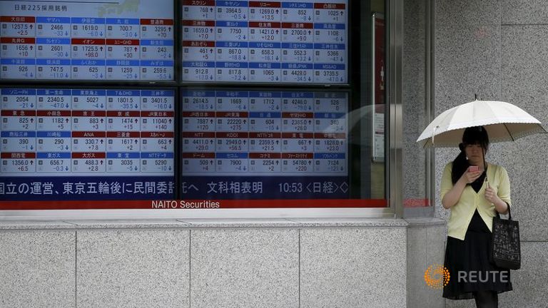 A woman looks at her mobile phone next to a stock quotation board outside a brokerage in Tokyo