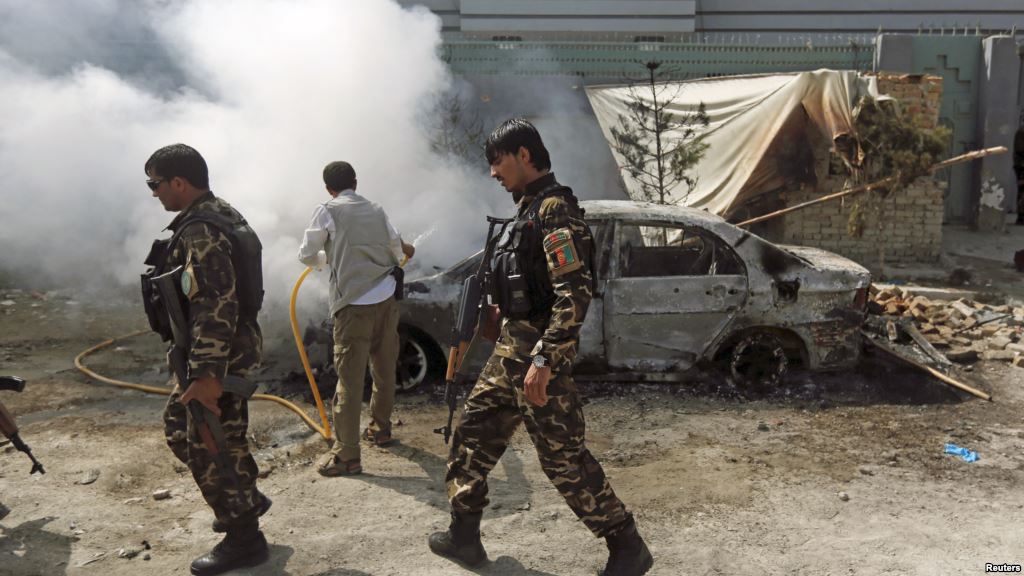 Afghan security forces walk past a burning car after a group of Taliban insurgents stormed a compound used by Afghanistan's intelligence agency in Kabul Afghanistan