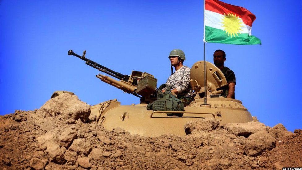 A flag at the autonomous Kurdistan region flies next to Iraqi Kurdish Peshmerga fighters