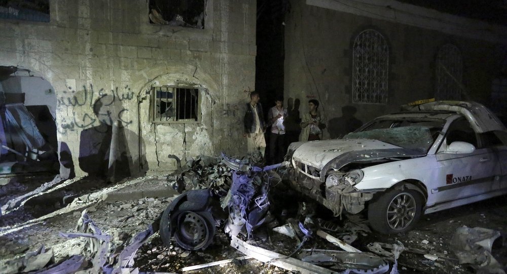 People stand next to wreckage at the site of a car bomb attack in Yemen's capital Sanaa