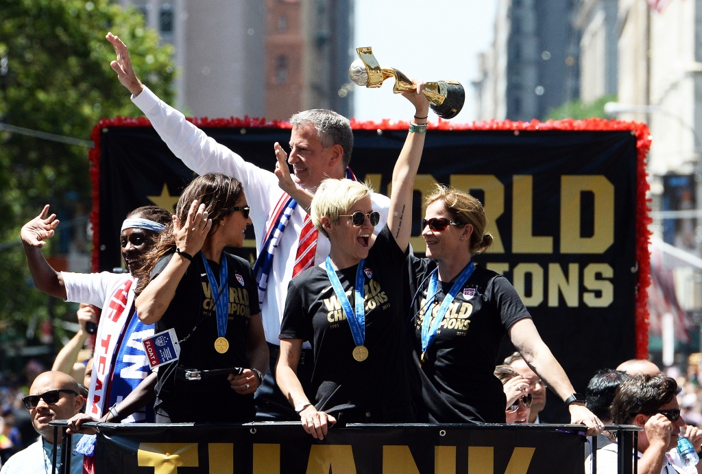 USA women's soccer team midfielder Megan Rapinoe holds up the World Cup 2015 trophy as midfielder Carli Lloyd, New York City Mayor Bill de Blasio and head coach Jill Ellis wave to the crowd during the ticker tape parade in New York