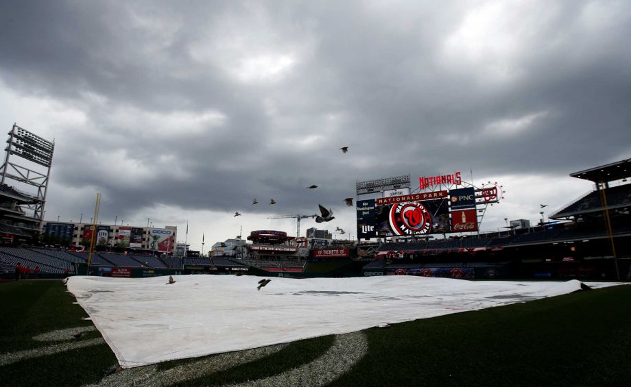 Birds fly over the tarp on the field as the rain falls before a baseball game between the Washington Nationals and the Cincinnati Reds at Nationals Park Wednesday