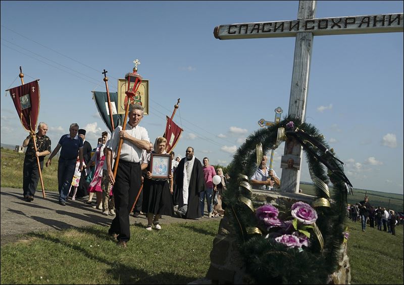 A religious procession passes an Orthodox cross with a sign reading Save and Guard at the crash site of the Malaysia Airlines Flight 17 near the village of Hrabove eastern Ukraine today