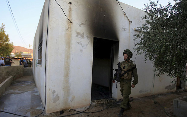 An Israeli soldier walks past a house that had been torched in a suspected attack by Jewish extremists killing an 18-month-old Palestinian child injuring a four-year-old brother and both their parents at Kafr Duma village near the West Bank city of Nablu