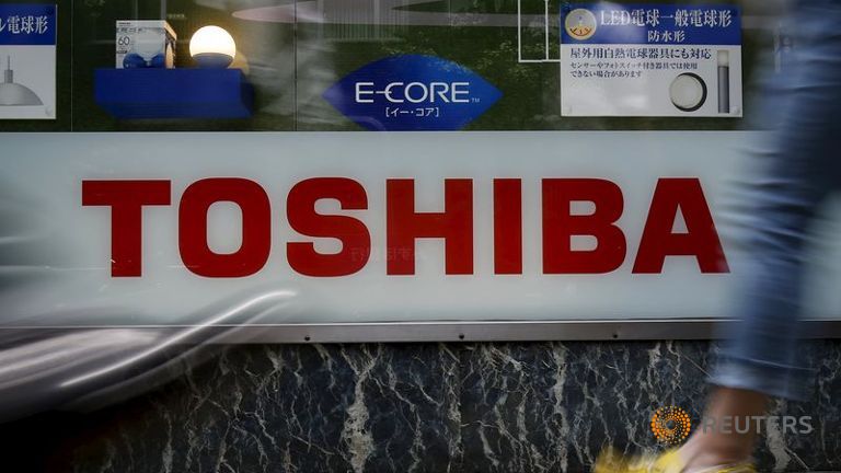 Pedestrians walk past a logo of Toshiba Corp outside an electronics retailer in Tokyo Japan