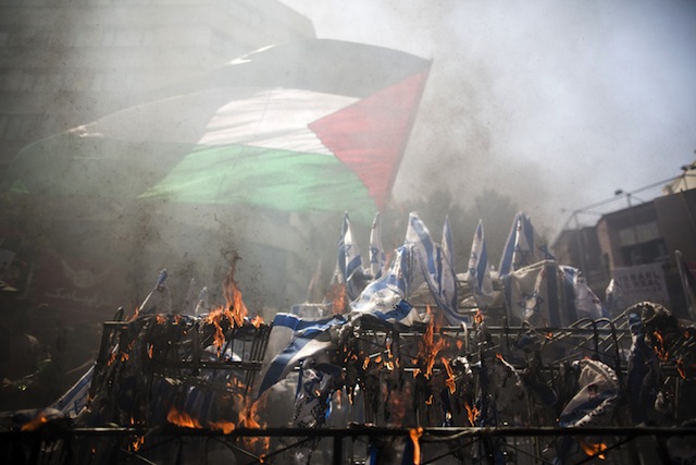 Iranian protestors wave a Palestinian flag over burning Israeli flags during a demonstration in Tehran