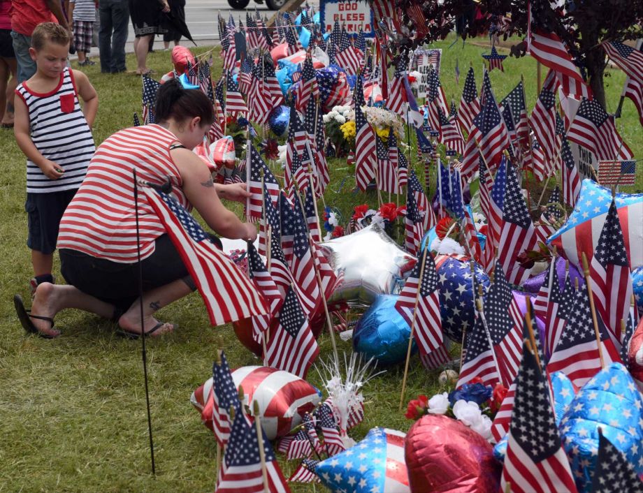 Isaac Pierce watches his mother Stefanie Pierce as she straightens an American flag at a makeshift memorial at the Armed Forces Career Center Sunday