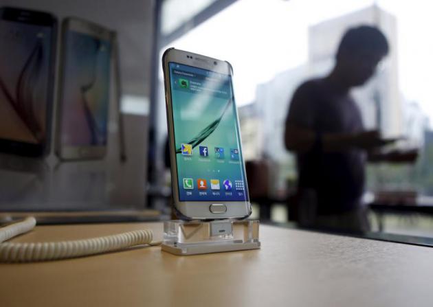 A customer using his phone walks past a Samsung Electronics&#039 smartphone Galaxy 6 at a store in Seoul