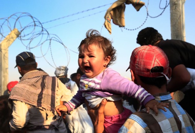 A Syrian refugee carries a baby after crossing over the broken border fence into Turkey from Syria.  Source PA