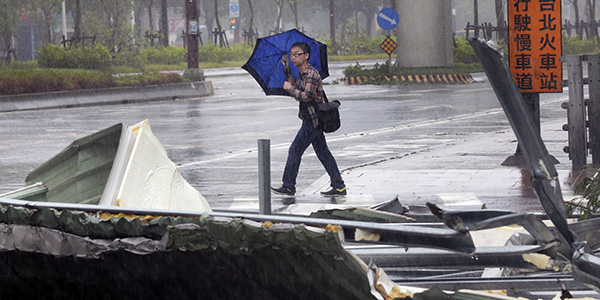 A man carrying an umbrella passes a mangled rooftop brought down by strong winds from Typhoon Soudelor in Taipei Taiwan Saturday. Pic AP