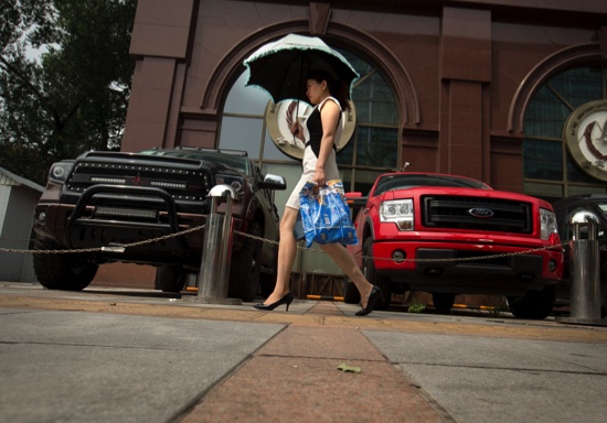 A woman walks past pickup trucks parked outside a luxury import car dealership in Beijing