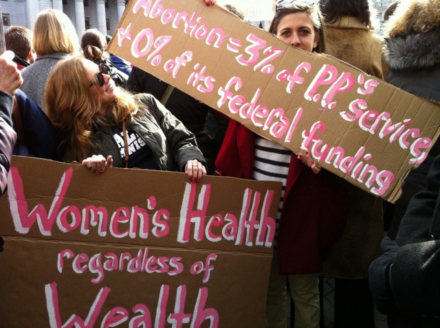 A woman at a rally holds up a sign to refute the pro-life argument against government funding for Planned Parenthood