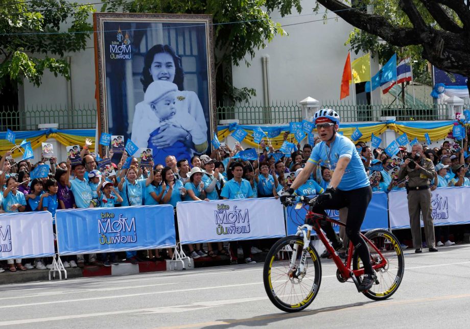 Thai Crown Prince Vajiralongkorn passes by a portrait of Queen Sirikit in Bangkok Thailand Sunday Aug. 16 2015. Thousands of cyclists pedaled through the streets of the Thai capital Sunday led by the country's crown prince on a 43-kilometer