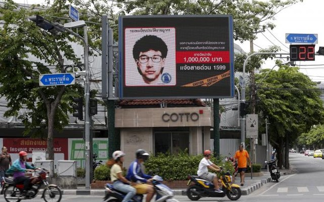 People ride their motorcycles past a digital billboard showing a sketch of the main suspect in Monday's attack on Erawan shrine in Bangkok Thailand