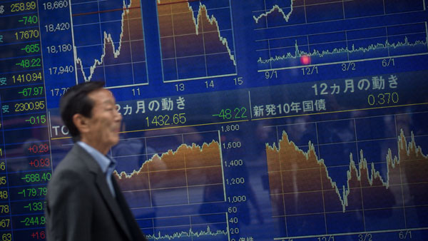 A man walks past a screen showing global stock market information on the street in Tokyo on Tuesday Aug. 25 2015