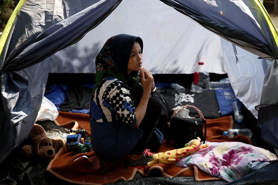 A migrant sits inside a tent at a park as she waits to be transferred along with other migrants to a organized camp which has been set up by the Greek state a few miles from the centre of Athens Sunday Aug. 16 2015. Greek authorities say they have star