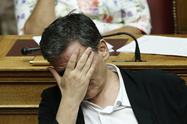 Greek Finance Minister Euclid Tsakalotos covers his face during a parliamentary session in Athens early Friday Aug. 14 2015. The Greek government defended its new bailout program in tumultuous parliamentary sessions as it faced a rebellion in the gover