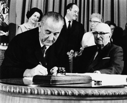 President Lyndon Johnson signs the Medicare Bill into law while former President Harry S. Truman right observes during a ceremony at the Truman Library in Independence Mo. At rear are Lady Bird Johnson Vice Pre