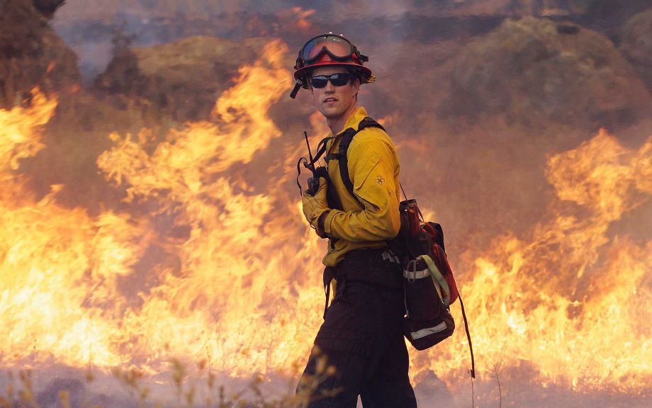 Garden Valley firefighter Chris Schwegler walks by flames along Morgan Valley Road near Lower Lake Calif. Thursday Aug. 13 2015. Crews battling the wind-stoked blaze took advantage of cooler temperatures Thursday to clear brush and expand containment