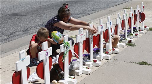 While her 6-year-old grandson Ace stays by her side Kathi Darciprette right hangs a marker back on the cross for Micayla Medek one of the victims of the massacre in a nearby movie theatre after writing a message on a heart handing from the cross