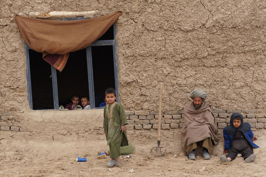 Members of a family sit outside their simple home in northern Afghanistan's Faryab province