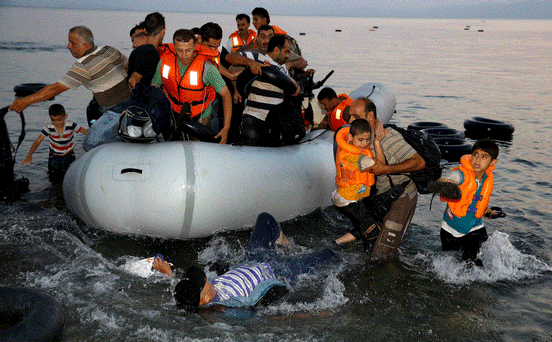 Syrian refugees carry their children as they jump off an overcrowded dinghy upon arriving yesterday on a beach on the Greek island of Kos after crossing part of the Aegean Sea