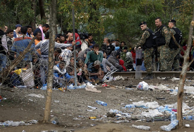 Migrants stand behind the barbed wire set by Macedonian police to stop thousands of migrants entering Macedonia illegally from Greece near the southern Macedonian town of Gevgelija Saturday Aug. 22 2015. About 39,000 people mostly Syrian migrants