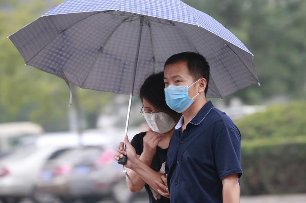 A couple wearing face masks shelter from the rain under an umbrella on a street that is more than 4km from the site of the explosions