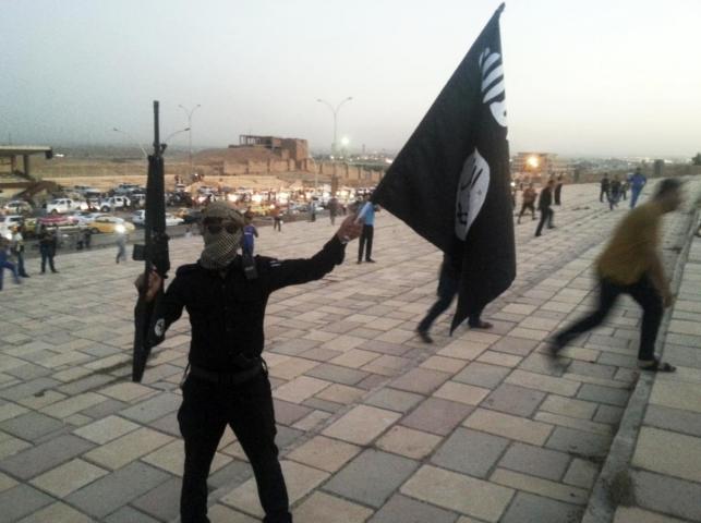 A fighter of the Islamic State of Iraq and the Levant holds an ISIL flag and a weapon on a street in the city of Mosul