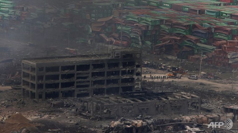 Rescuers walk past a damaged building at the site of the explosions in Tianjin