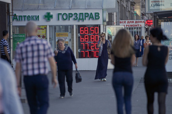 People walk past an exchange office sign showing the currency exchange rates in Moscow Russia Friday Aug. 21 2015. The Russian ruble currency is falling under the pressure of cheaper oil reviving concerns over the country's economic outlook. (AP Phot