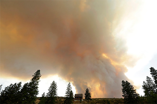 Smoke from an approaching wildfire looms over a home near Twisp Wash. where three firefighters have been killed