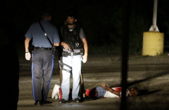 Police stand near a suspect in a Ferguson Mo. parking lot after gunfire during a protest on the anniversary of the death of Michael Brown