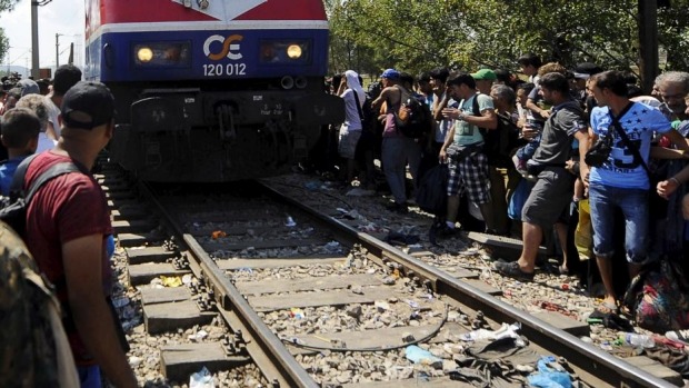 Migrants sitting along a railway track on the Greek side of the border move away as a train approaches the Greek Macedonian border