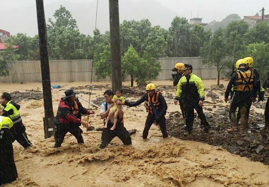 In this image released by the New Taipei Fire Department emergency rescue personnel carry a child through a flash mudslide caused by Typhoon Soudelor in Xindian New Taipei City northern Taiwan Saturday Aug. 8 2015. At least four people were killed