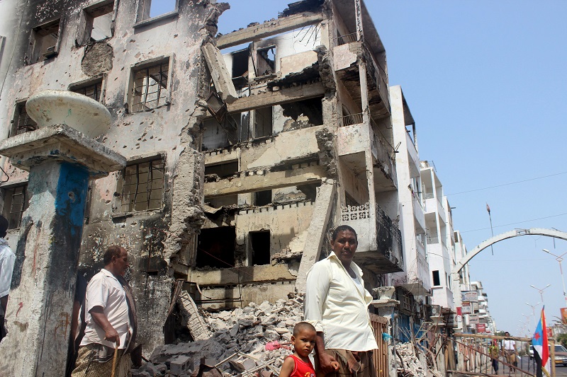 People walk past a building damaged by recent fighting between Houthi militants and fighters of the Southern Resistance in Yemen's southern port city of Aden pic