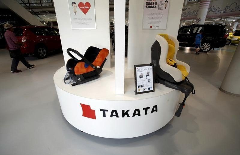 Visitors look at cars behind a logo of Takata Corp on its display at a showroom for vehicles in Tokyo Japan