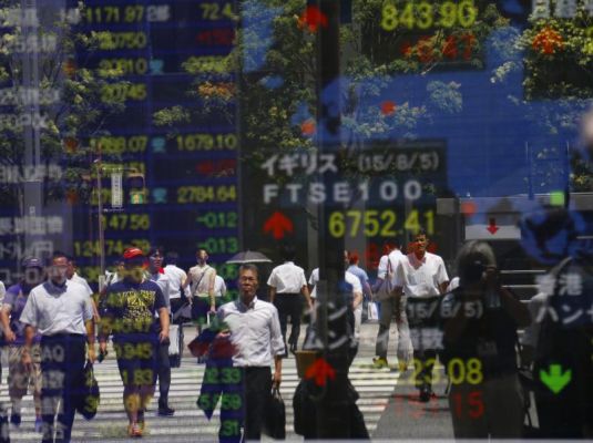 People are reflected on an electronic stock indicator