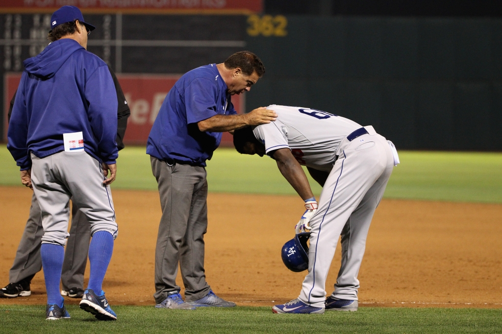 Yasiel Puig #66 of the Los Angeles Dodgers is looked at by a trainer in the eighth inning of their game against the Oakland Athletics