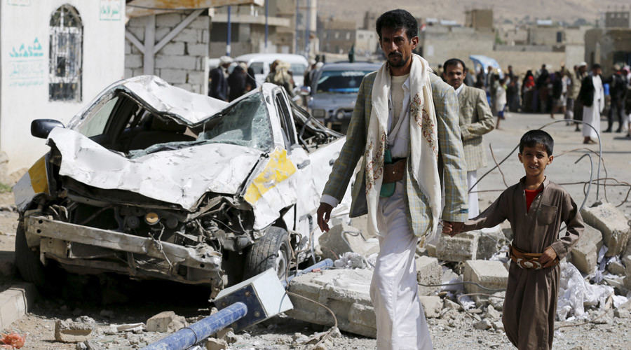 A man and his son walk past a car destroyed by Saudiled air strikes on the nearby offices of the education ministry's workers union in Yemen's northwestern city of Amran