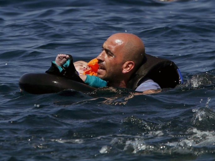 A Syrian asylum-seeker holding a baby in a lifetube swims towards the short after their boat sank before reaching Lesbos