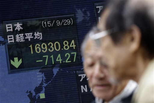 Men walk past an electronic stock board of a securities firm in Tokyo Tuesday Sept. 29 2015. Asian stock markets tumbled Tuesday extending a global market sell-off triggered by grim corporate news expectations of a Fed rate hike and jitters about Chi