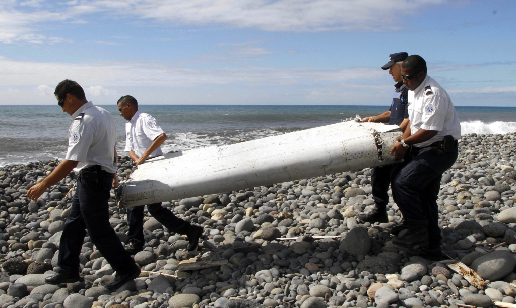 French officers carry a wing fragment called a flaperon that washed ashore in La Réunion island in the Indian Ocean on July 29