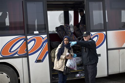 A Croatian police officer shows the way to a woman as she exits a bus in front of a registration center for migrants and refugees in Opatovac Croatia Thursday Sept. 24 2015. Serbia has banned imports of Croatian goods and Croatia has retaliated by bar