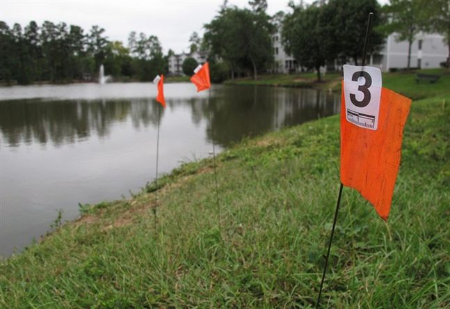 Orange evidence flags line the shore of a pond in the Audubon Lake neighborhood of Durham N.C. on Tuesday Sept. 22 2015. Police say Alan Tysheen Eugene Lassiter attempted to drown his three young children two of whom remain hospitalized. (AP