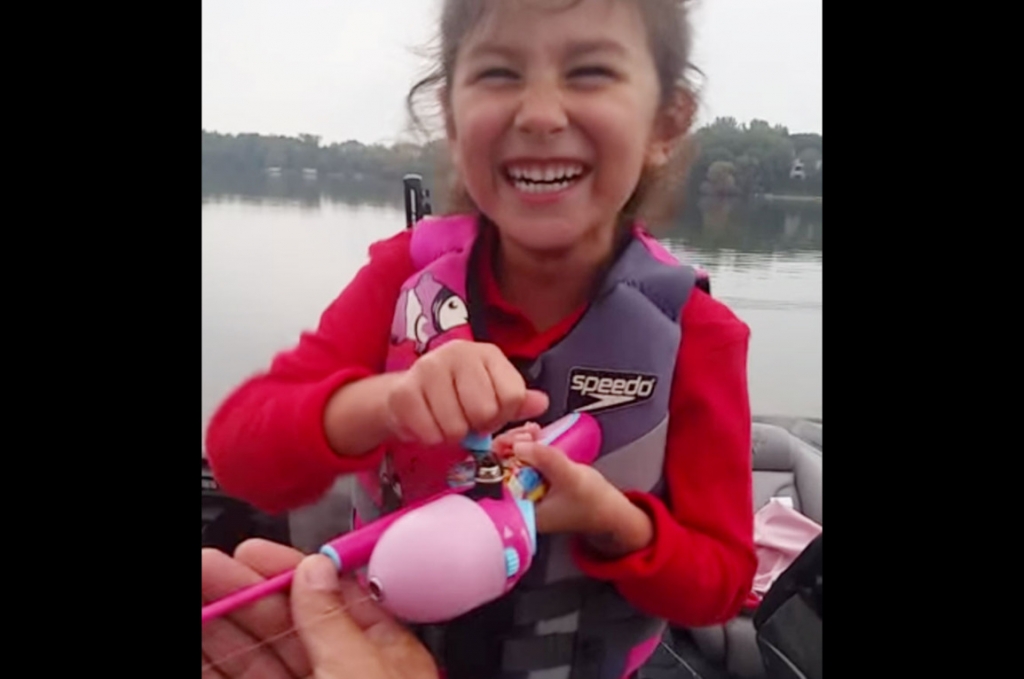 Dad encourages daughter as she catches a huge bass with her Barbie fishing rod