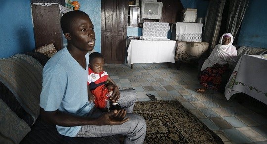 18 2015 nurse Donnell Tholley 25 holds his adopted son Donnell Junior at their apartment in Freetown Sierra Leone as the baby’s great-grandmother Marie looks on. Tholley adopted the boy following the death of the